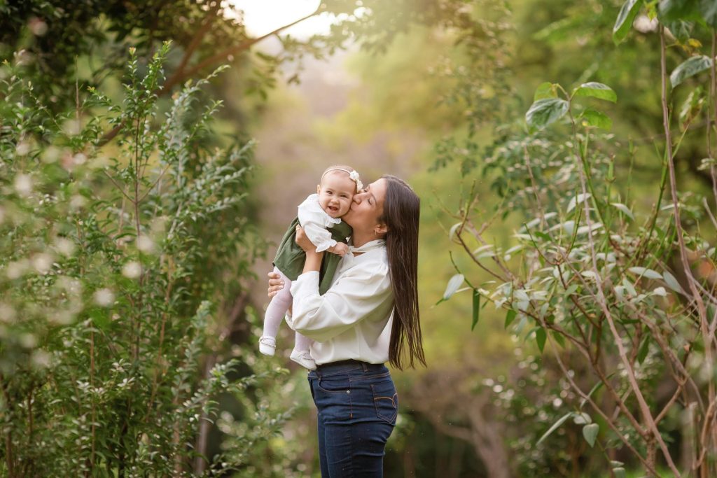 Joyful moment of a mother holding her smiling baby daughter in a lush green outdoor setting.